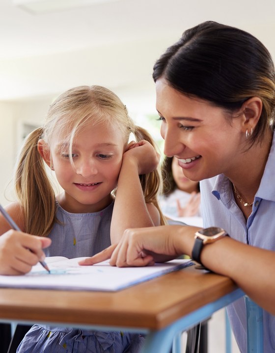 A teacher helping a young student with schoolwork in a bright classroom