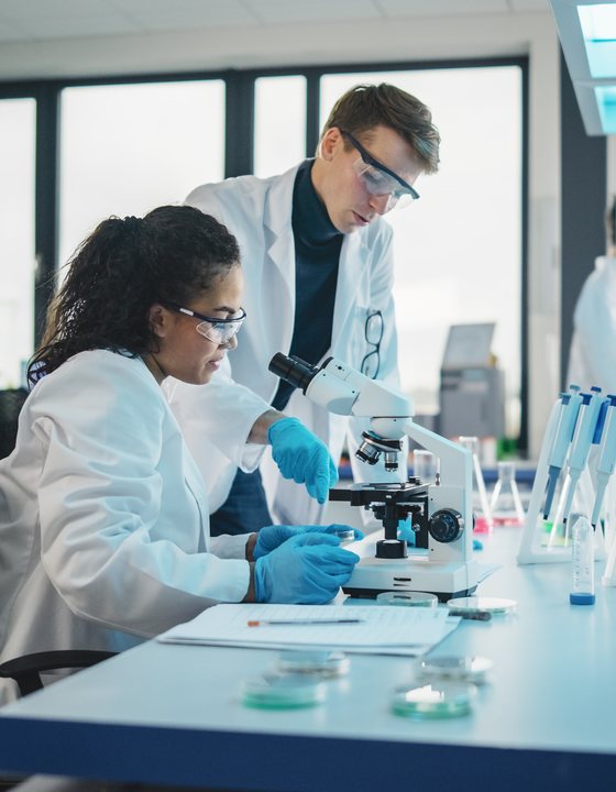 Two medical researchers examining samples under a microscope in a laboratory